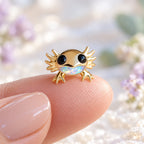 Boucles d'oreilles Axolotl Mopaline, posée sur le bout du doigt pour montrer la petite taille