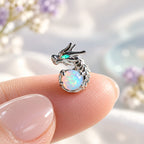 Boucles d'oreilles Dragon Mopaline, posée sur le bout du doigt pour montrer la petite taille