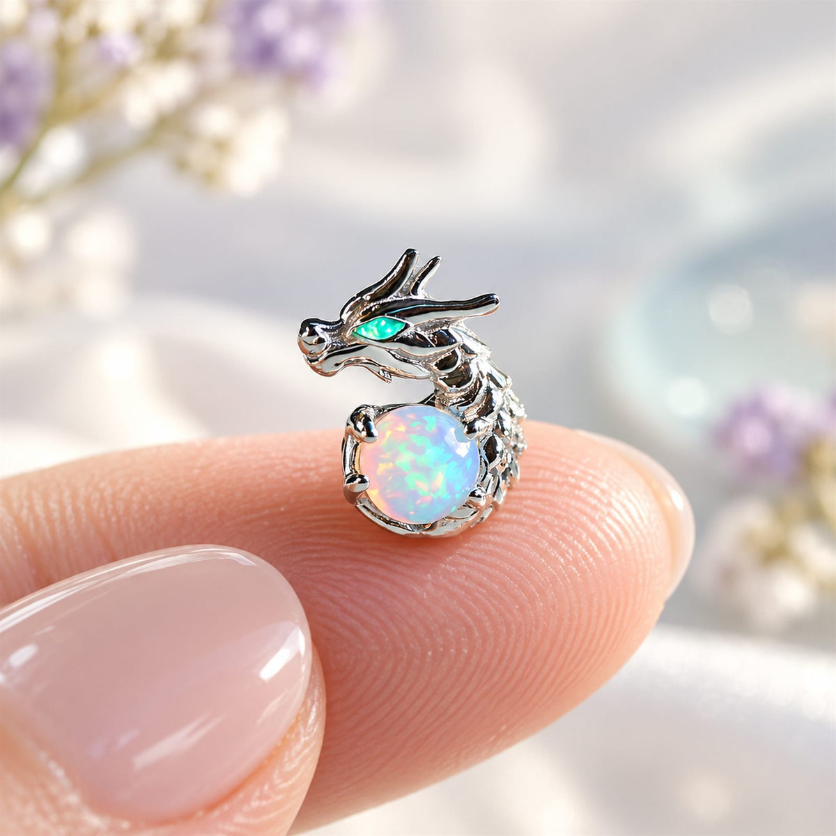 Boucles d'oreilles Dragon Mopaline, posée sur le bout du doigt pour montrer la petite taille