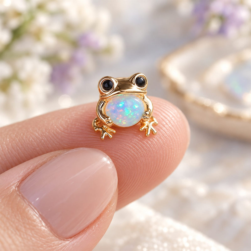 Boucles d'oreilles Grenouille Mopaline, posée sur le bout du doigt pour montrer la petite taille