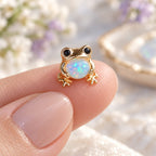 Boucles d'oreilles Grenouille Mopaline, posée sur le bout du doigt pour montrer la petite taille